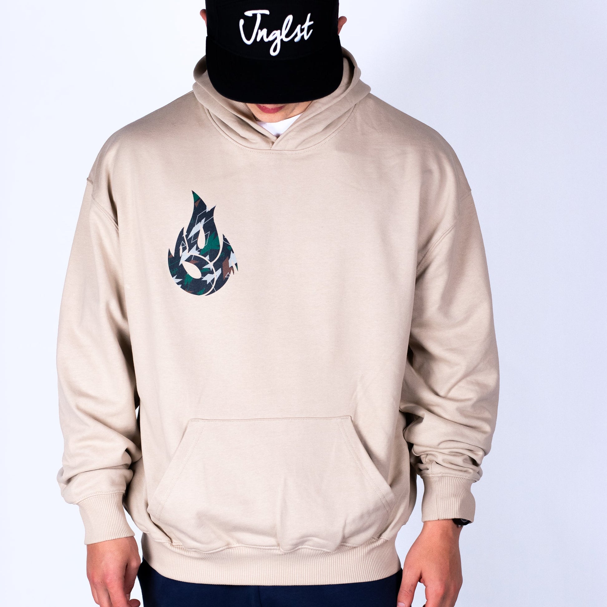 Person wearing a beige hoodie with a logo and a black cap with 'Jnglst' text on a white background