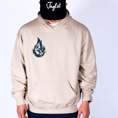 Person wearing a beige hoodie with a logo and a black cap with 'Jnglst' text on a white background