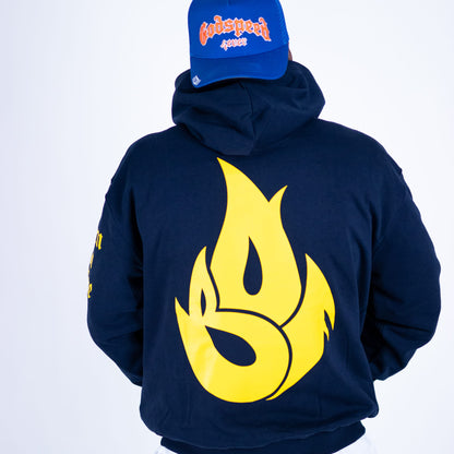 Person wearing a navy hoodie with a yellow flame design and a blue cap with red text on a white background