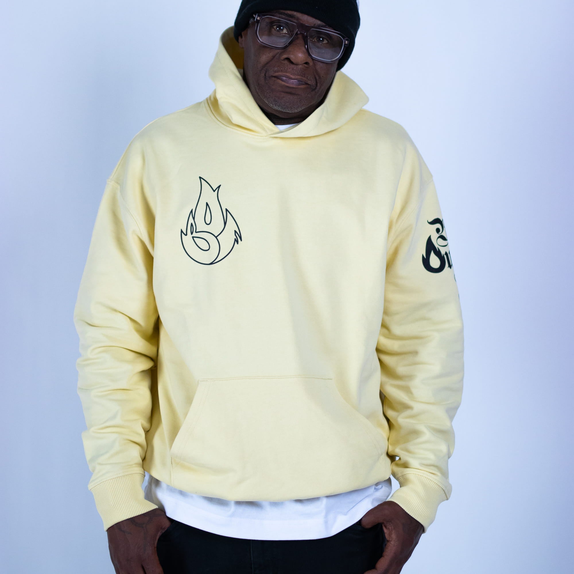Person wearing a light yellow hoodie with black designs on a plain background