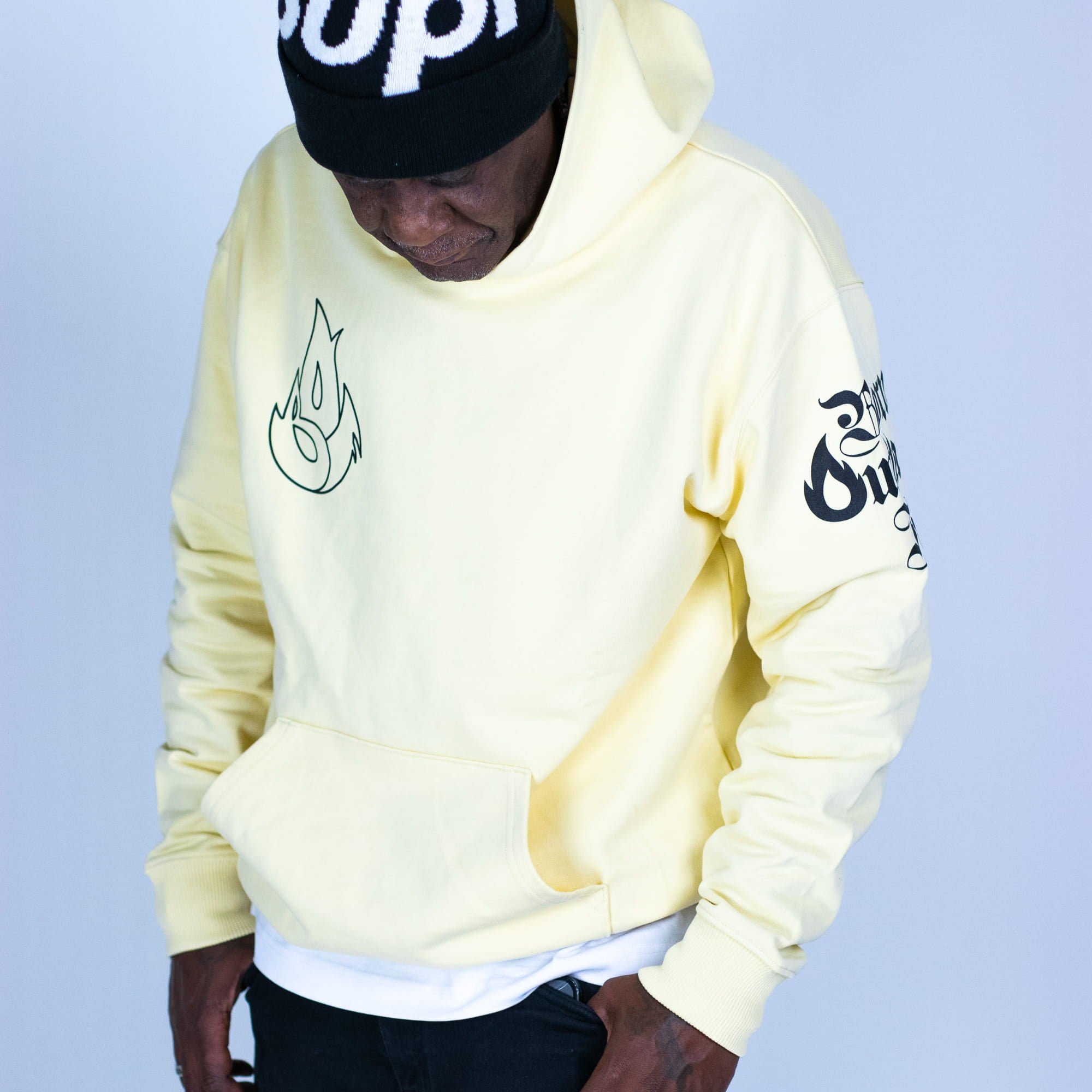 Person wearing a light yellow hoodie with branding on a plain background