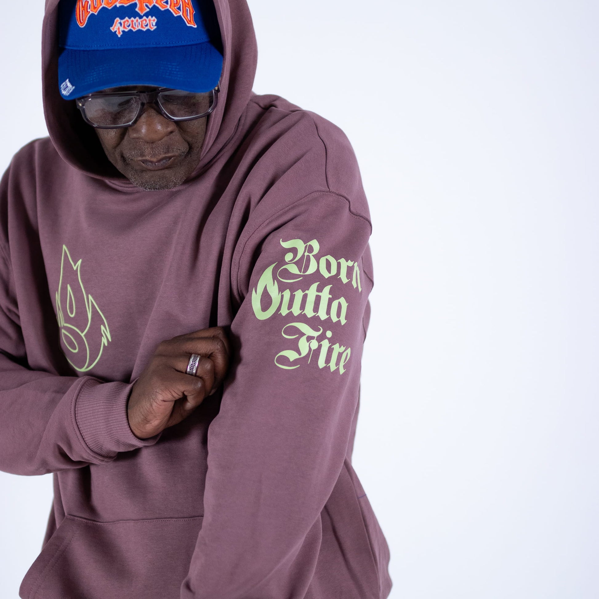 Person wearing a maroon hoodie with text and a blue cap on a white background