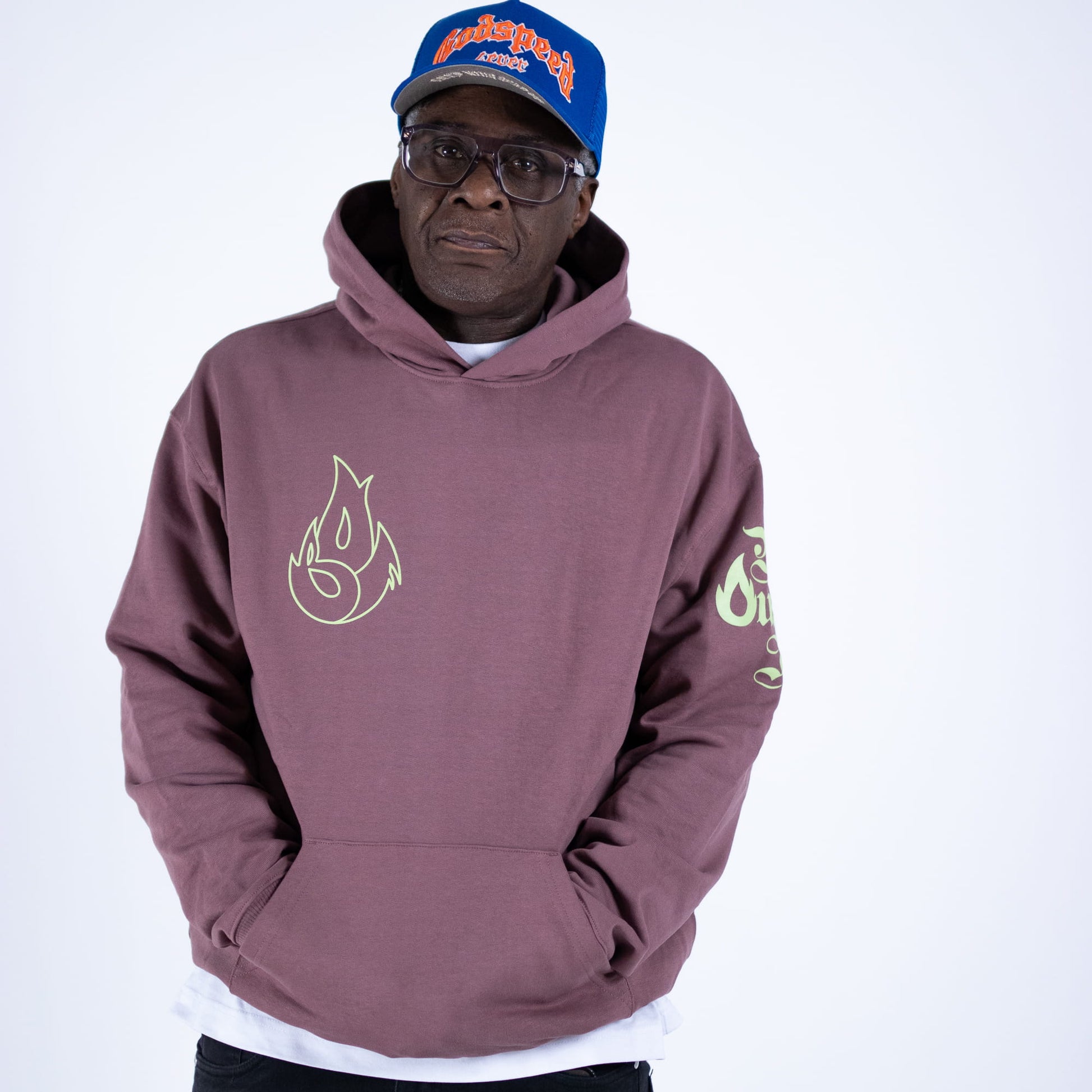 Man wearing a maroon hoodie with a flame design and a blue cap on a white background