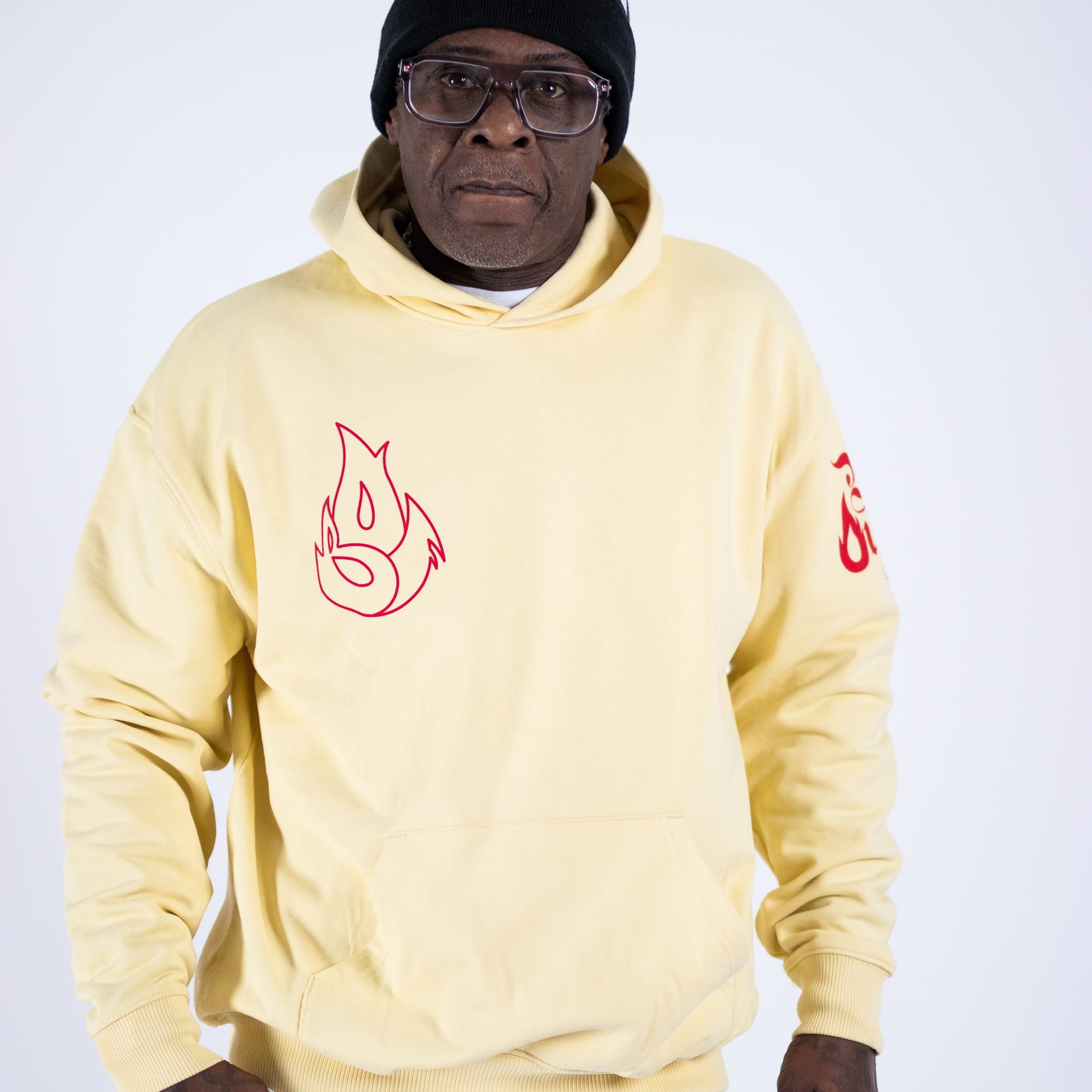 Man wearing a light yellow hoodie with red designs on a white background