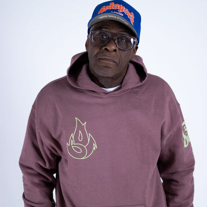 Man wearing a maroon hoodie with a flame design and a blue cap with red text on a white background