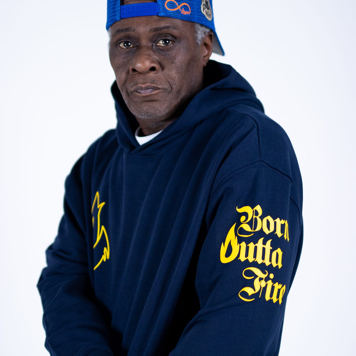 Person wearing a navy hoodie with yellow text and a blue cap on a white background