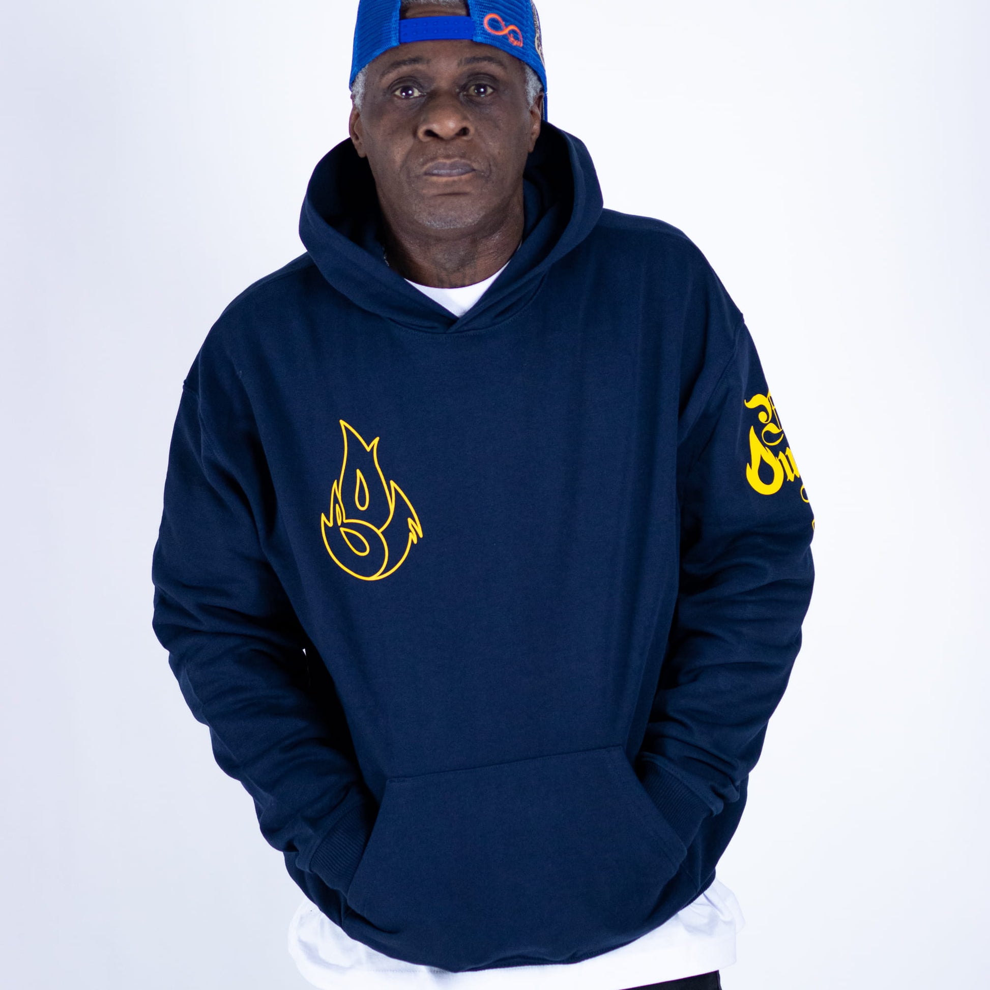 Man wearing a navy hoodie with yellow logo and blue cap on a white background
