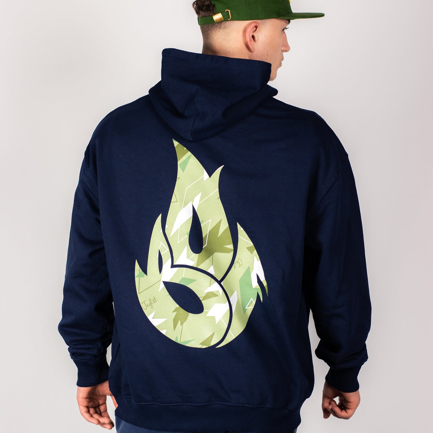 Person wearing a navy hoodie with a green camo flame design on the back against a plain background