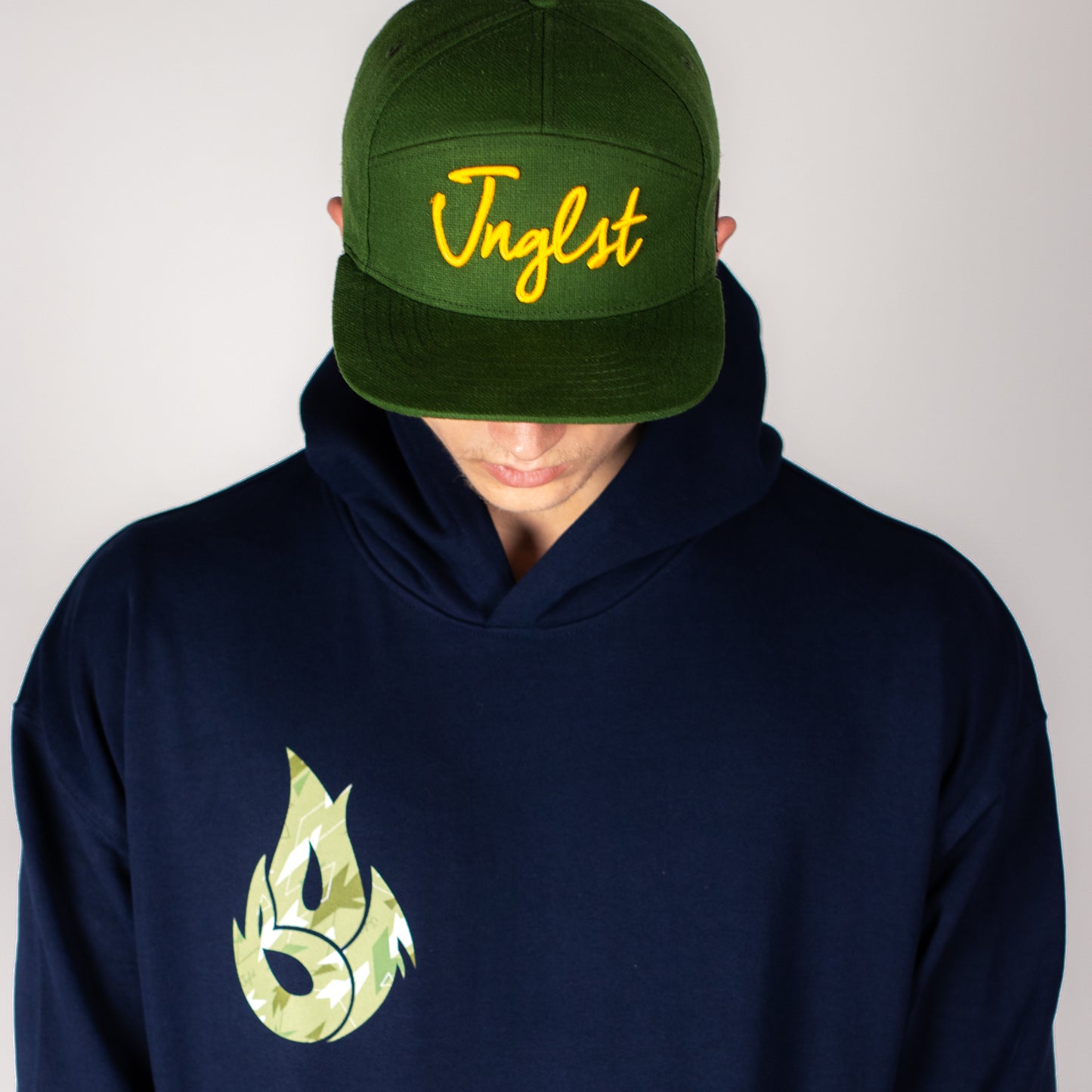 Person wearing a green cap with yellow text and a navy Born Outta Fire hoodie with a green logo on a plain background