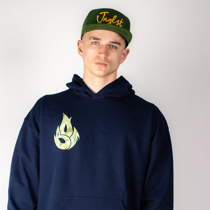 Person wearing a navy Jnglst hoodie with a logo and a green cap with text on a plain background