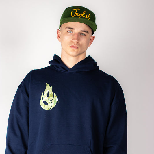 Person wearing a navy Jnglst hoodie with a logo and a green cap with text on a plain background