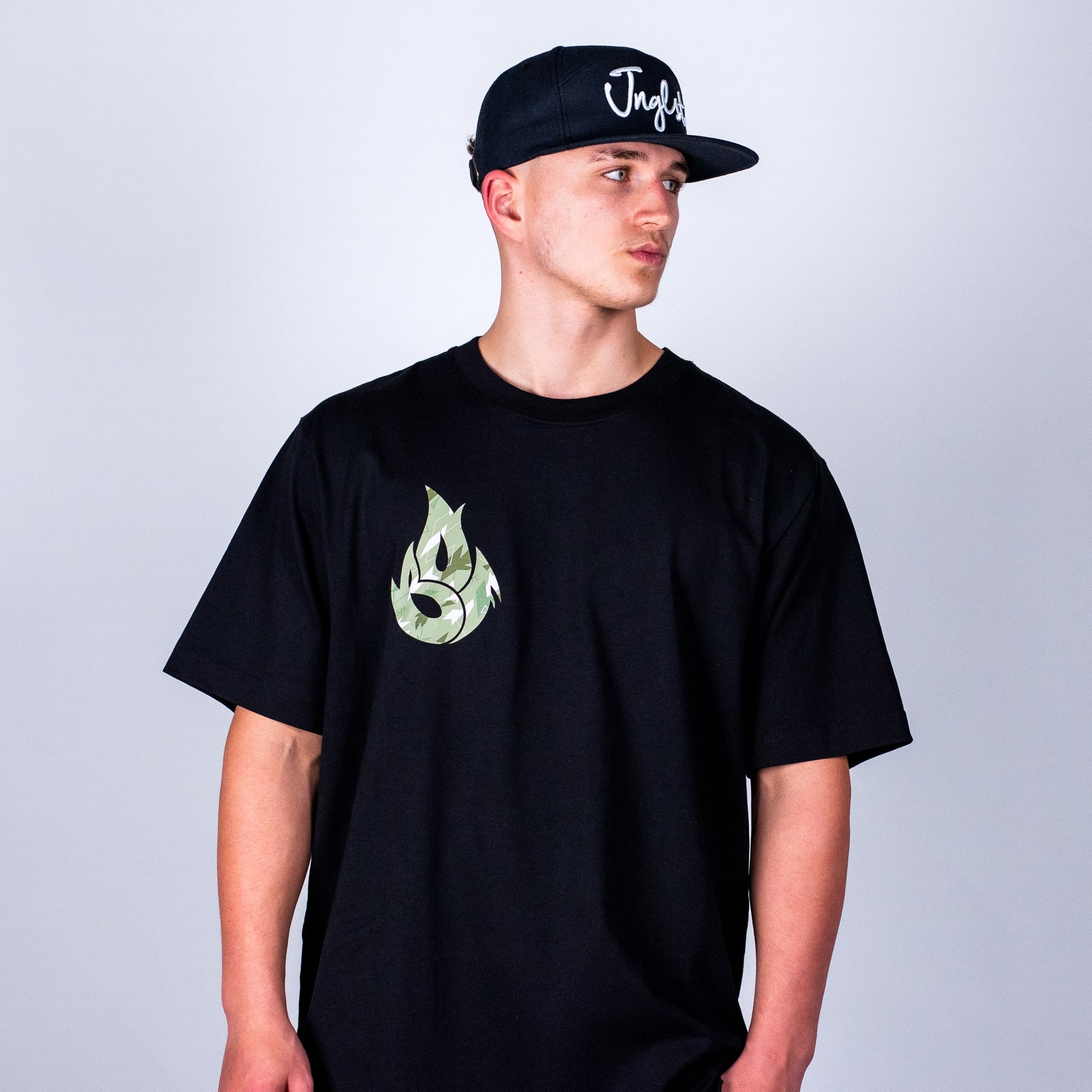 Person wearing a relaxed black t-shirt with a green logo and a black cap on a light grey background