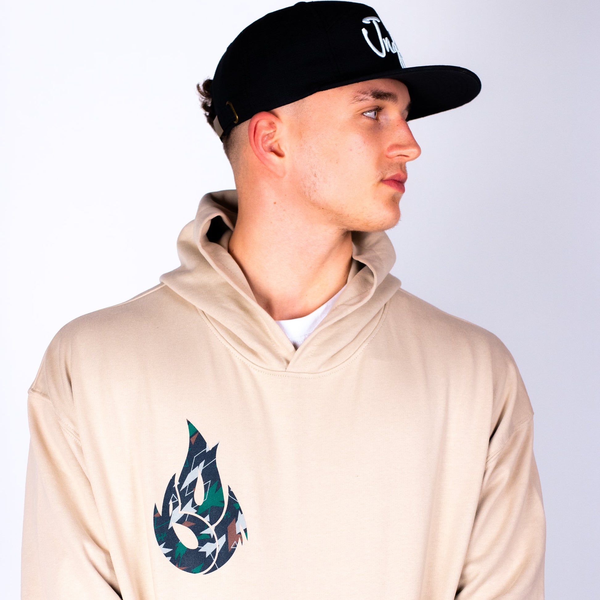 Man wearing a beige hoodie with a logo and a black cap on a white background